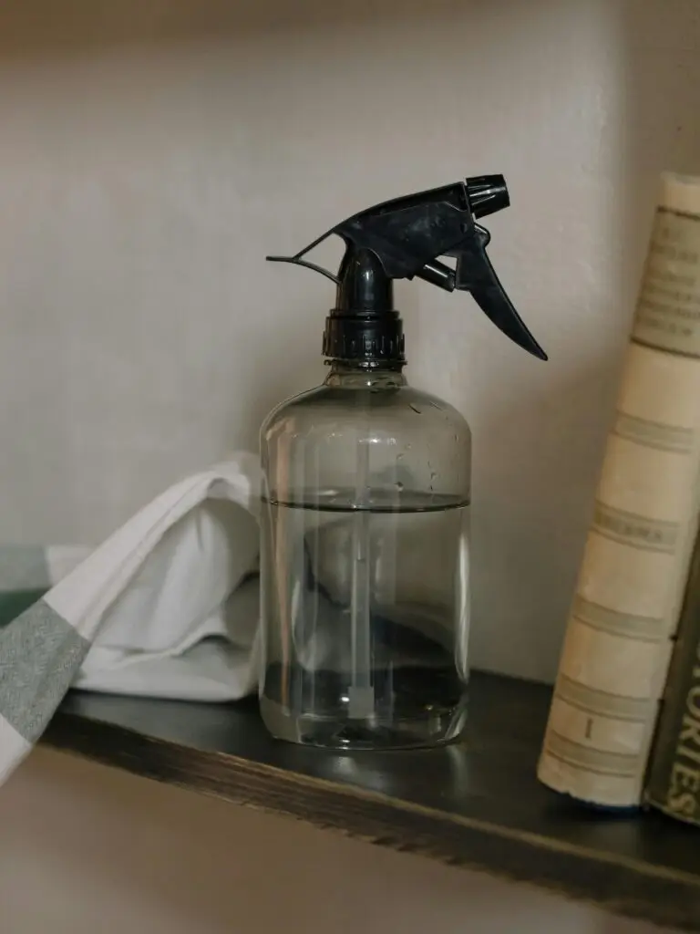 Close-up of a glass spray bottle on a shelf with a towel and books.